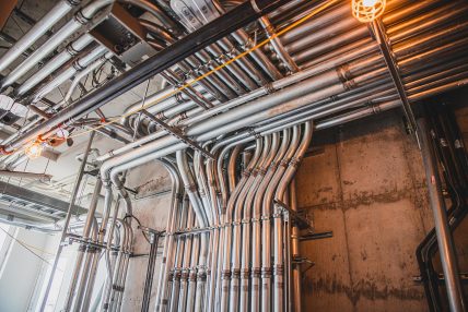 Installation professionnelle de conduits électriques rigides en métal dans un bâtiment commercial, sur un mur de béton, avec éclairage de chantier