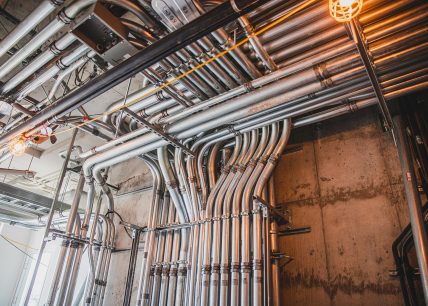 Installation professionnelle de conduits électriques rigides en métal dans un bâtiment commercial, sur un mur de béton, avec éclairage de chantier