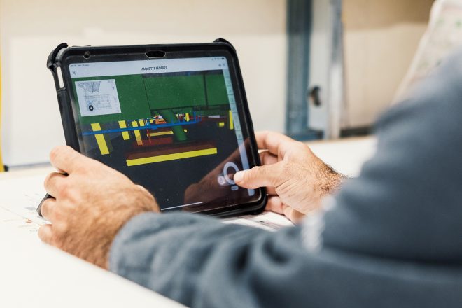 A worker views a 3D digital BIM model on a tablet, showing the mechanical systems of a building