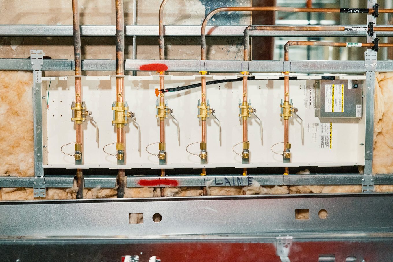 Medical gas distribution panel under installation, featuring copper piping, control valves, and exposed wall insulation