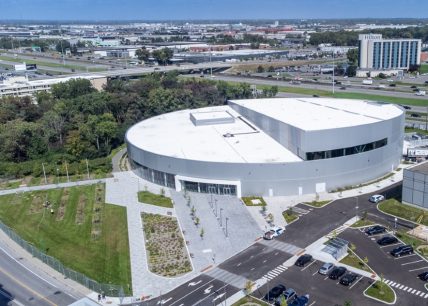 Vue aérienne du Complexe aquatique de Laval, montrant le bâtiment moderne à toit blanc, les aménagements paysagers, le stationnement et l’autoroute en arrière-plan