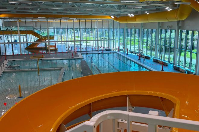 Vue intérieure du Complexe aquatique de Laval avec piscine intérieure, toboggan jaune et grandes baies vitrées laissant entrer la lumière naturelle