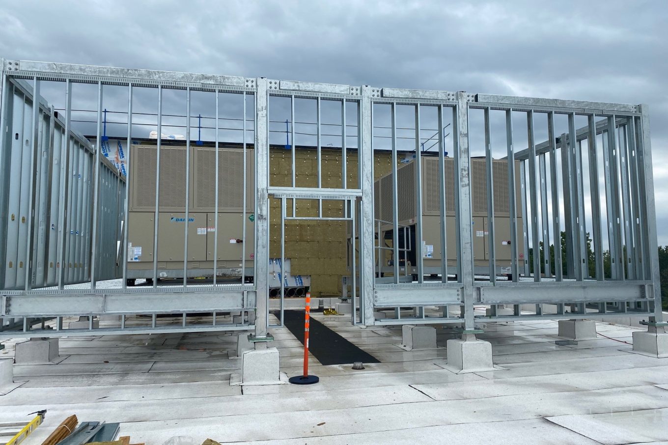 Mechanical equipment installation on a rooftop, with galvanized steel framing under construction and Daikin ventilation units in the background
