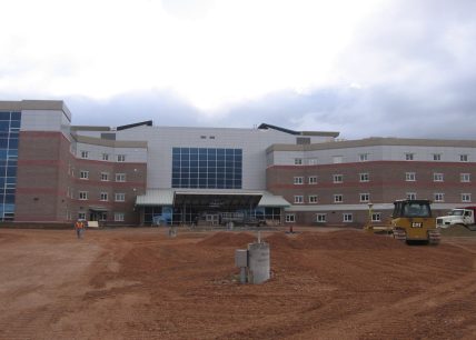 Hôpital en construction à Corner Brook avec machinerie lourde sur le chantier et façade moderne en briques et panneaux d’aluminium