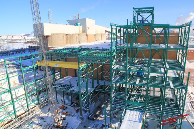Structure d'acier verte en construction sur le site minier de Mont-Wright en hiver, avec grue, neige au sol et bâtiments industriels en arrière-plan