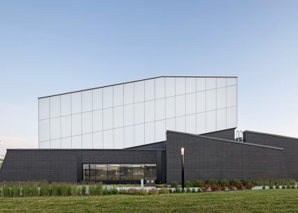 Vue extérieure de la station Côte-Vertu de la STM, montrant un bâtiment à l’architecture moderne avec façade noire texturée, volume supérieur blanc et aménagement paysager soigné