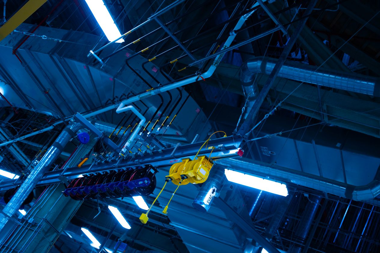 Industrial mechanical room with piping labeled HPL and ERR, neon lighting, and complex overhead ventilation systems